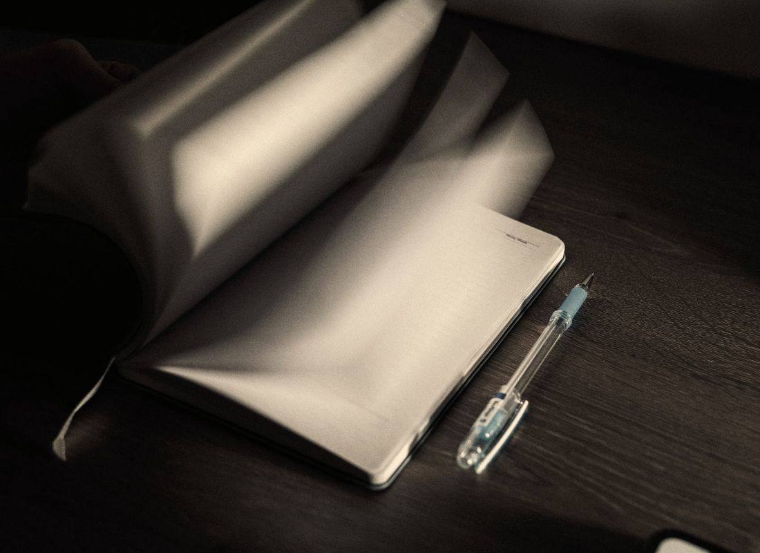 An open notebook, blank, and a pen on a dark table.